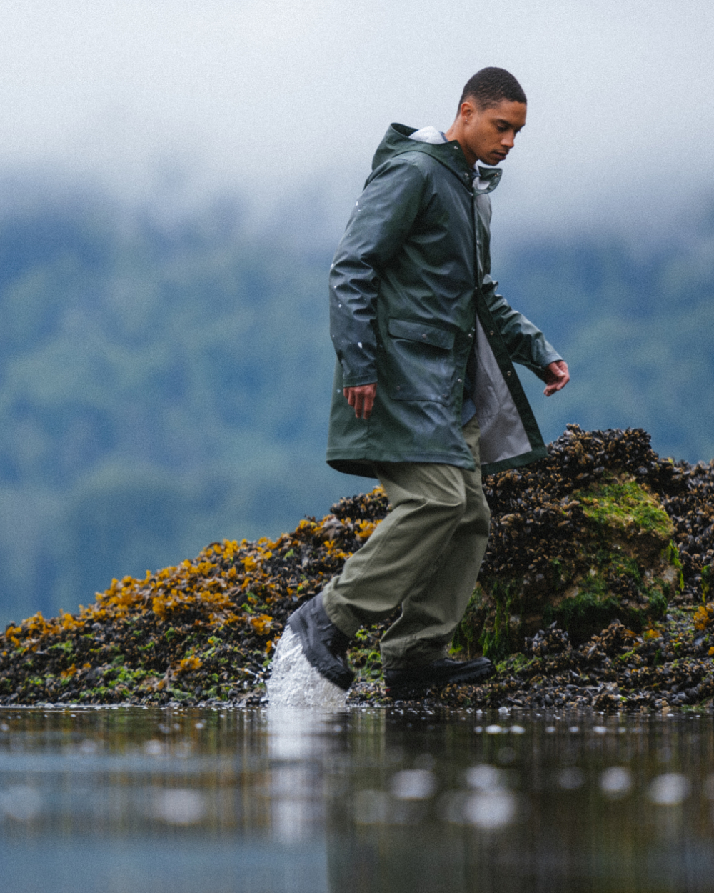 A person walking through the water along the shore in the Herschel Supply Company x Sperry Authentic Original 3-Eye Lug shoes in Black