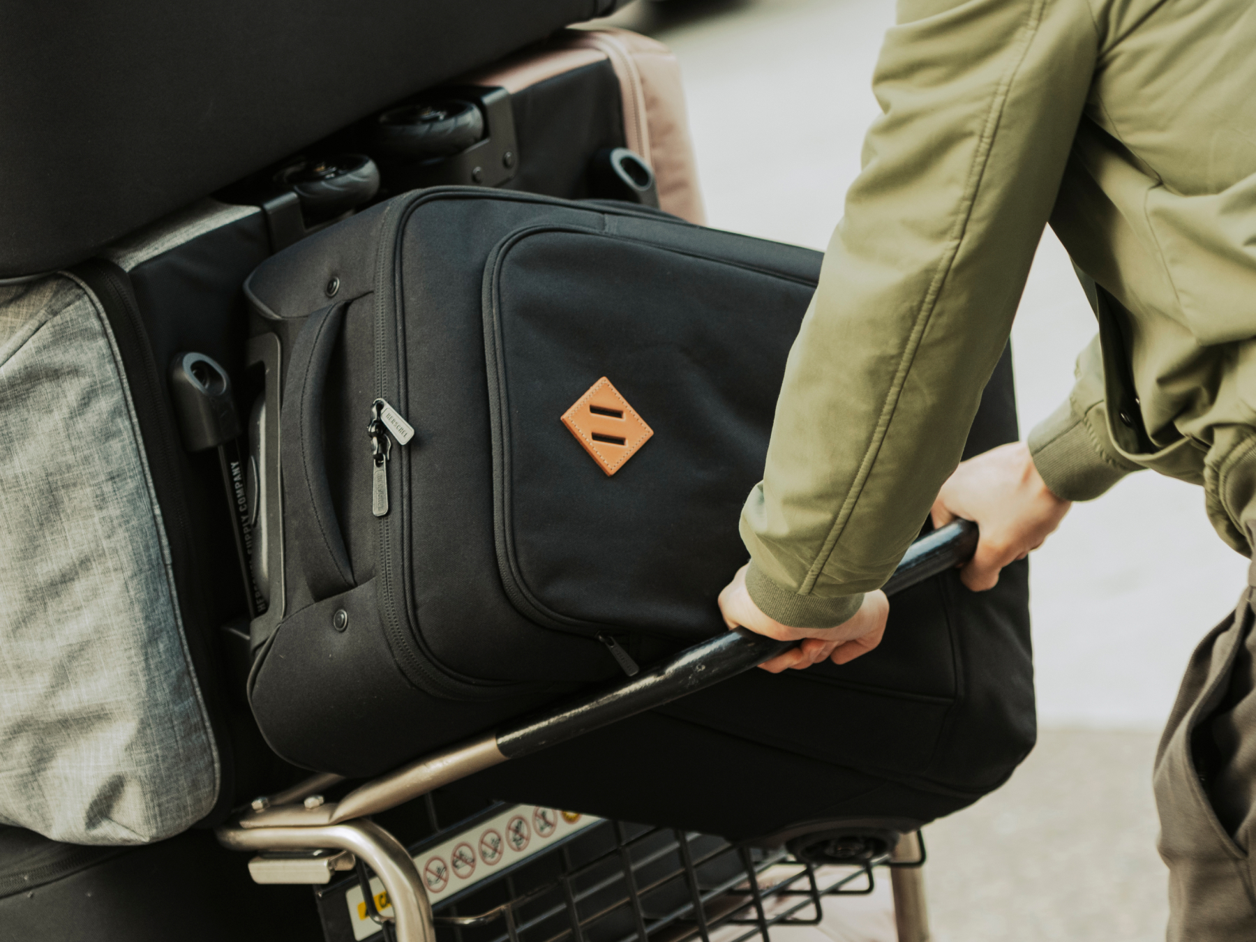 A Herschel Heritage® Softshell Large Carry-On Luggage in black being pushed in an airport luggage cart.